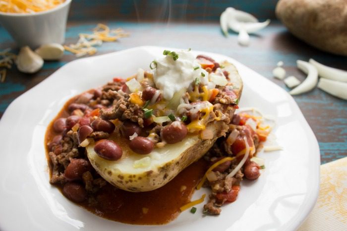 A chili cheese baked potato on a white plate with steam coming off it