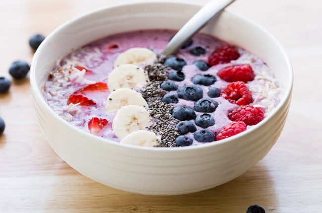 A white bowl filled with smoothie and fruit sitting on a wooden surface