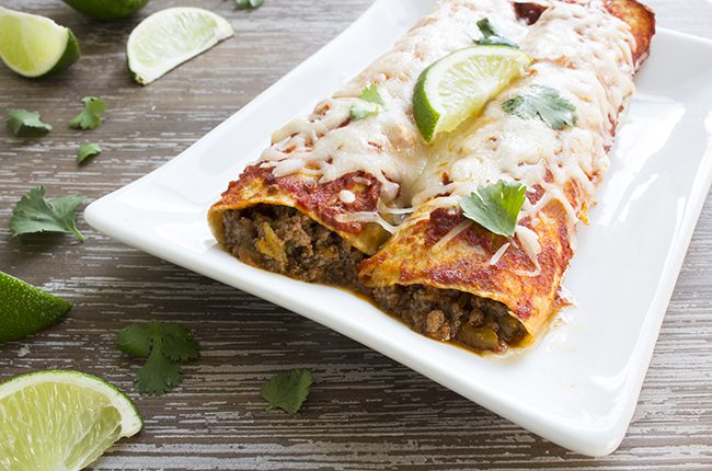 Enchiladas on a white plate topped with cheese and slice of lime