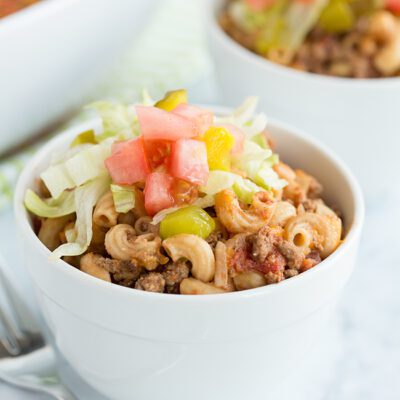 Up close picture of a bowl of cheeseburger casserole topped with lettuce pickle and tomato