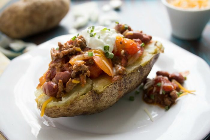 Up close picture chili cheese baked potato on white plate with sour cream