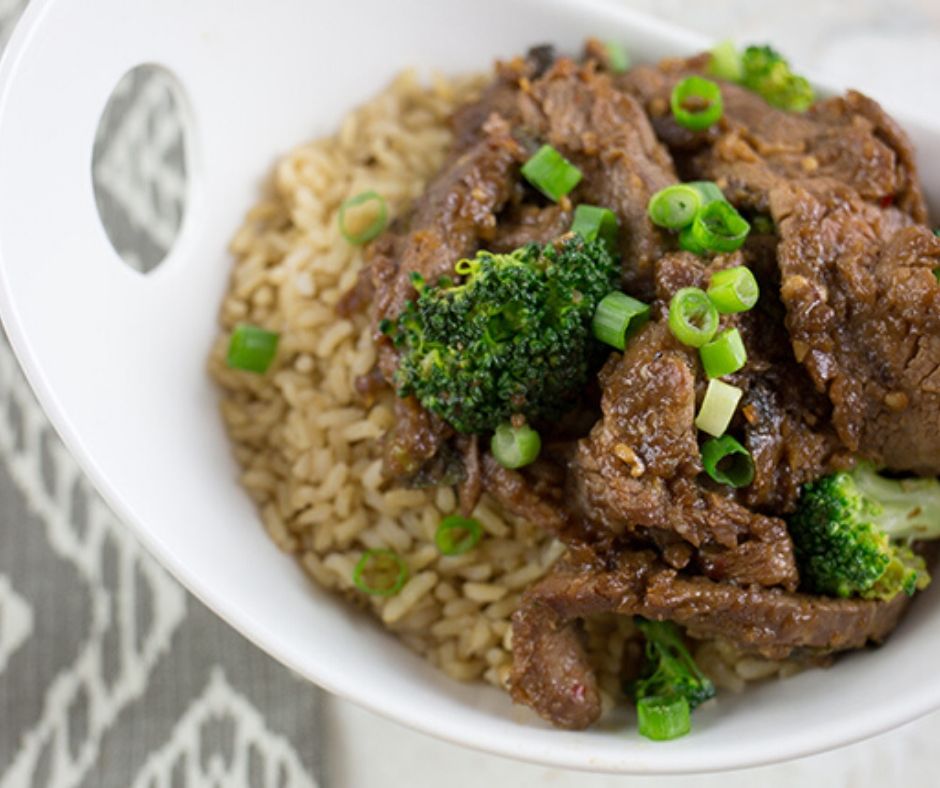 Up close picture of beef strips with broccoli in a bowl over brown rice