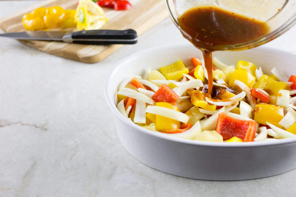 bell peppers and onions in dish pouring over sauce for baked sweet and sour chicken recipe