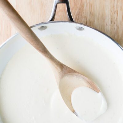 Light alfredo sauce being stirred with a wooden spoon in a stockpot