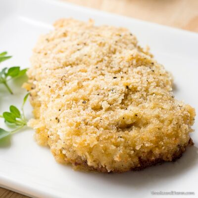 Parmesan pork chop on white plate with parsley