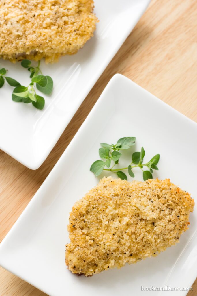 Parmesan pork chop on white plate with parsley