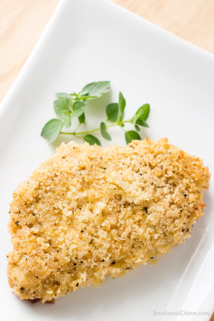 Parmesan pork chop on white plate with parsley