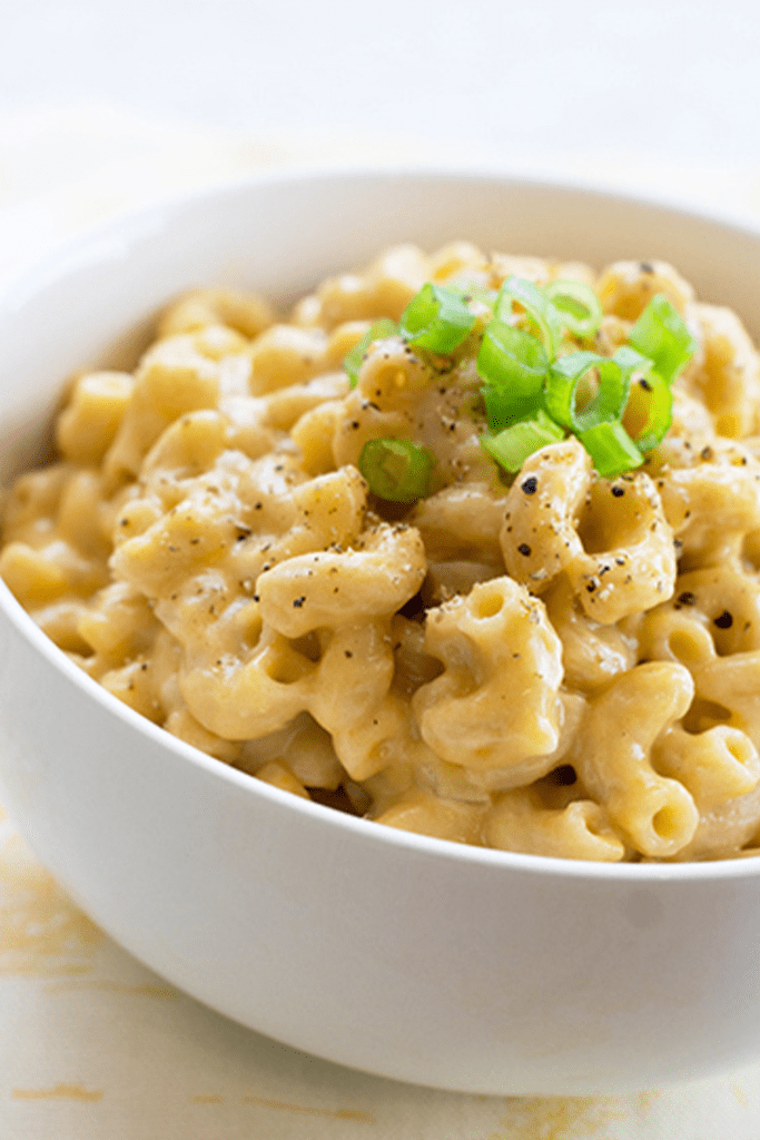 Up close picture of a white bowl filled with healthy mac and cheese topped with chives and black pepper
