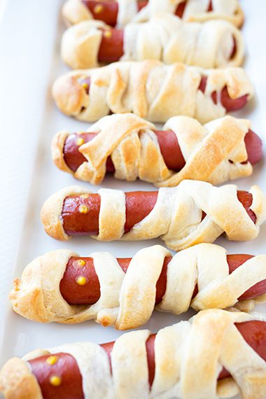 Long white platter full of mummy hot dogs