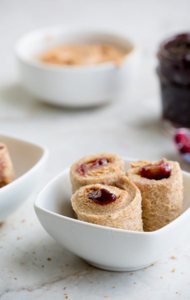 White table with bowls of peanut butter and jelly sushi rolls