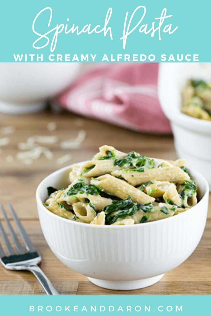 A large white bowl of spinach pasta on a wooden table with fork beside the bowl