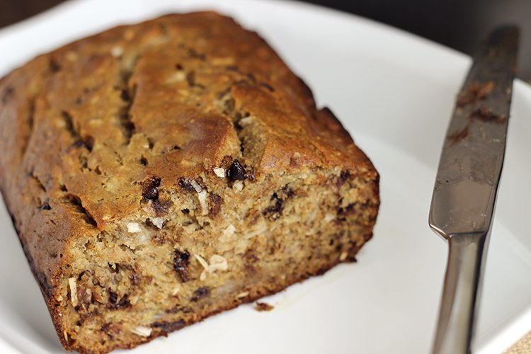 A loaf of coconut banana braed on a white plate being sliced