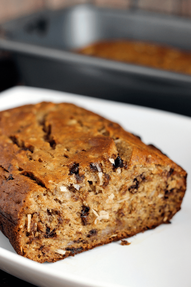 A loaf of coconut banana bread with chocolate chips on a white plate