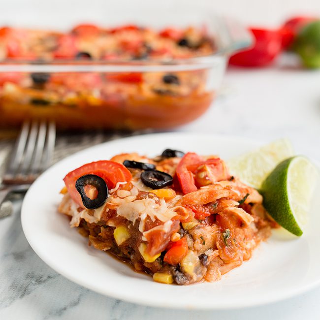 A serving of taco casserole mexican lasagna on a white plate in front of baking dish