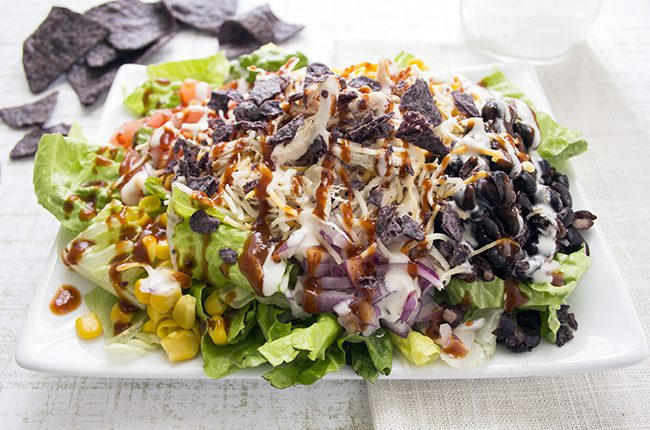 An up close picture of a plate of barbecue chicken salad topped with onions black beans corn and shredded chicken