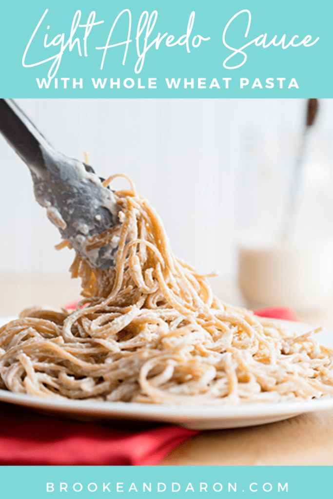 Light alfredo sauce on whole wheat pasta sitting on a white plate on a red napkin