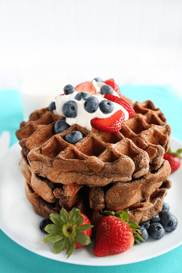 Long picture of a plate of chocolate waffles topped with berries and cream