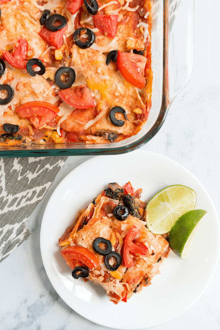 Overhead picture of a casserole with a white plate and mexican lasagna portion with sliced limes