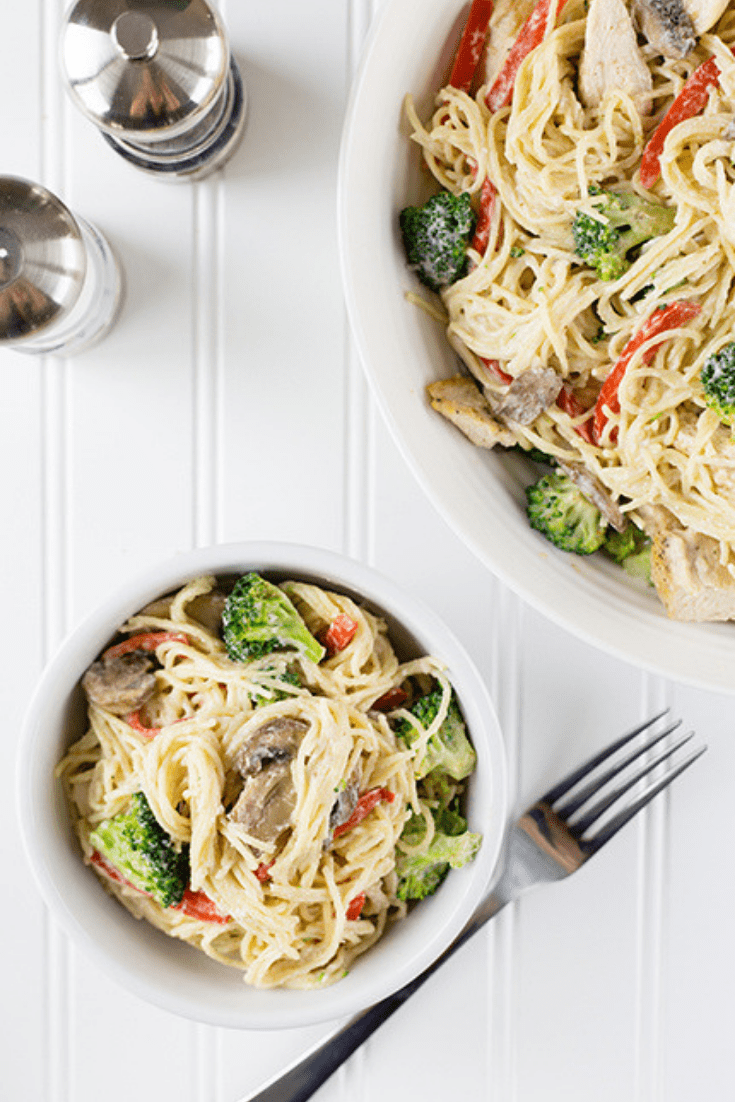 Overhead picture of a small white bowl filled with chicken primavera pasta on a white table