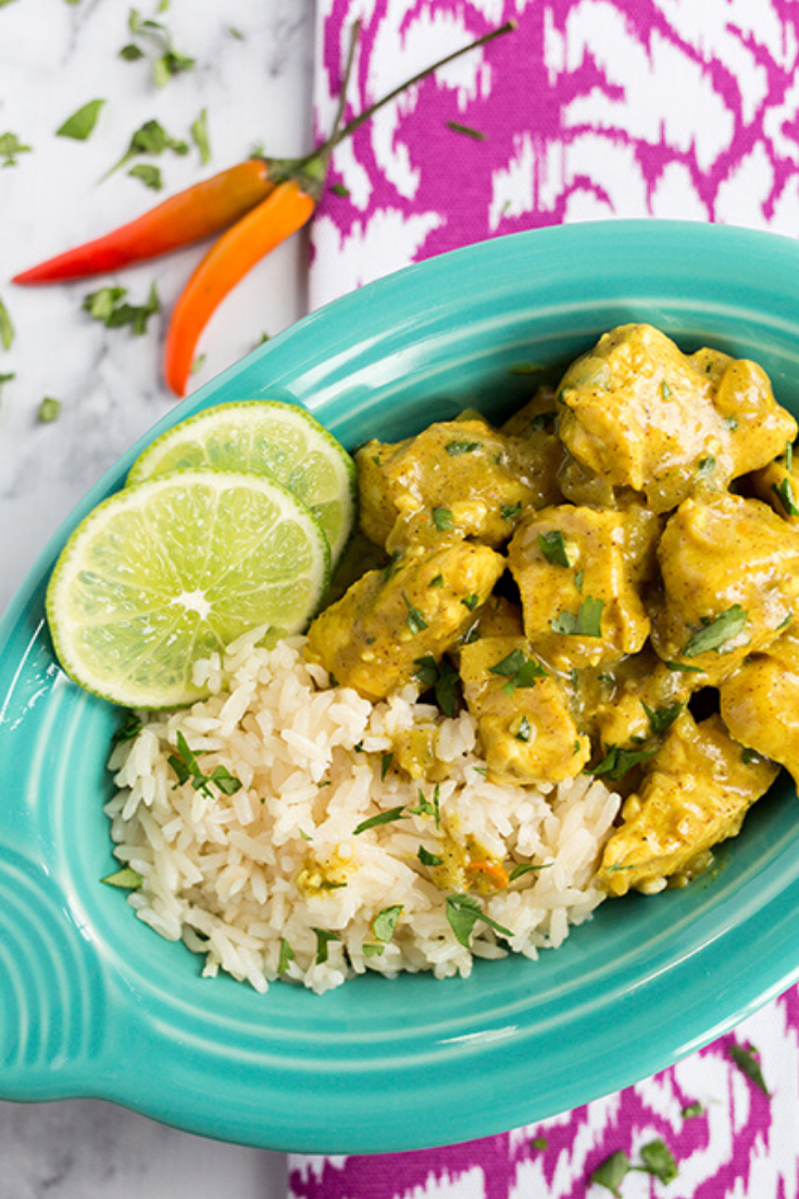 Overhead picture of a teal bowl on marble counter filled with thai curried chicken and rice