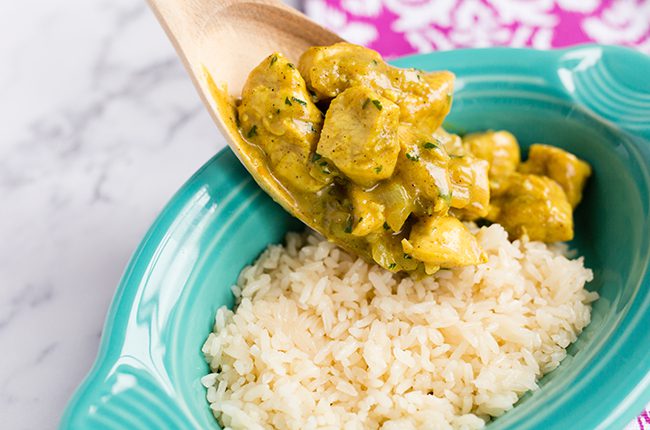 Overhead picture of a wooden spoon pouring thai chicken into a teal bowl filled with rice