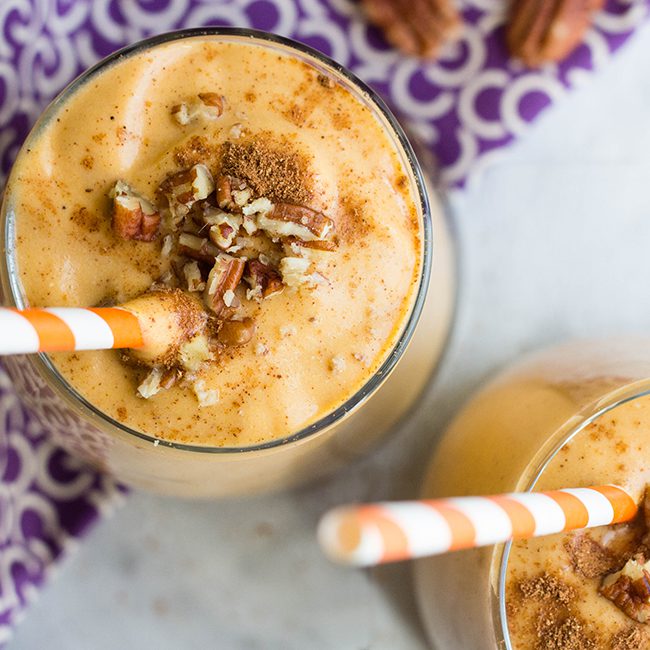 Overhead close up picture of pumpkin smoothie in glasses sitting on a purple cloth