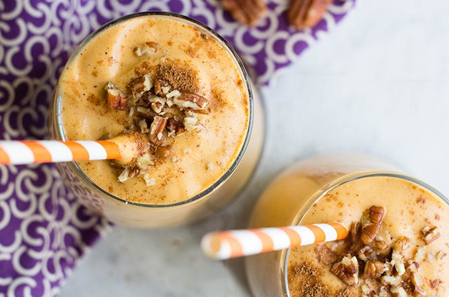 Overhead picture of two glasses of pumpkin smoothie on white counter with purple cloth in background