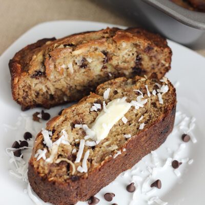 Two slices of banana bread with coconut and chocolate chips laying on a white plate