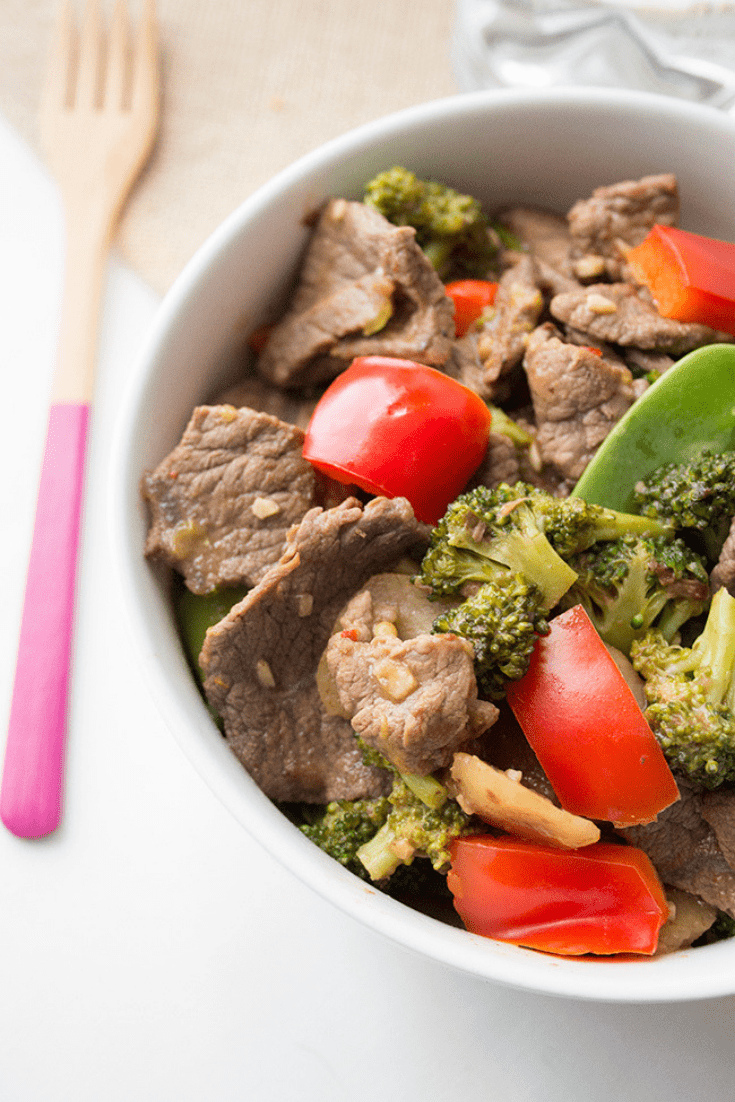 Up close picture of a large white bowl of Chinese beef stir fry with wooden fork on the side