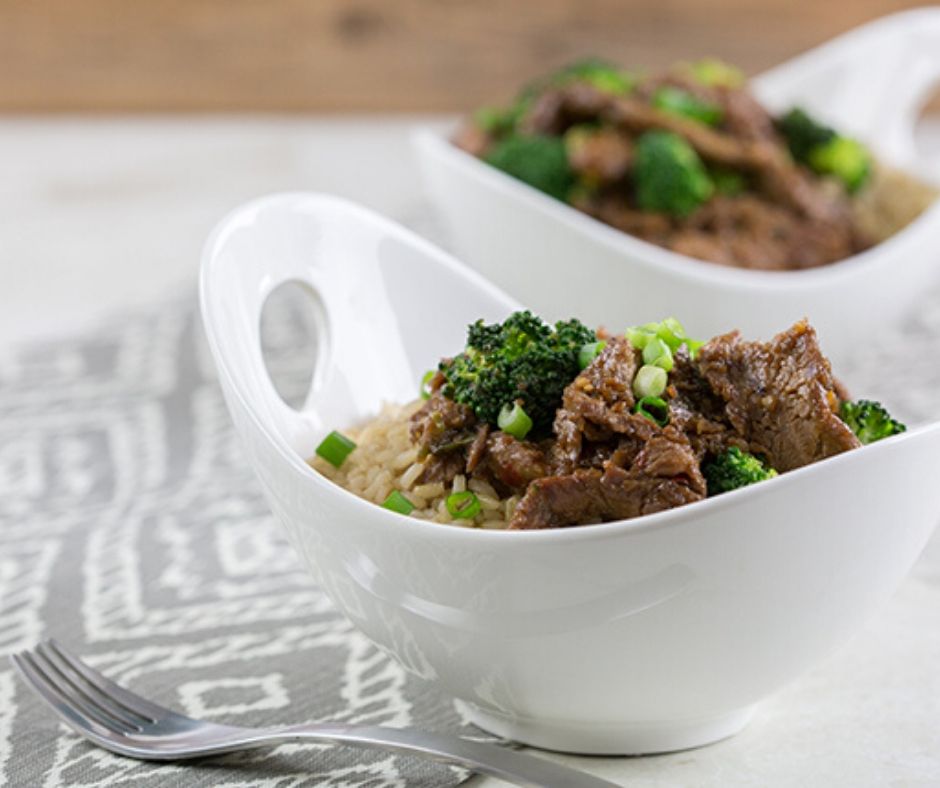 Two large white bowls filled with mongolian beef stir fry sitting on a gray table runner
